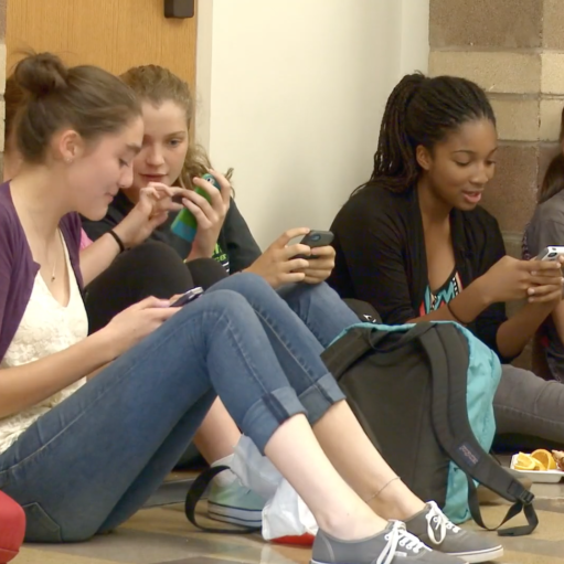Three students sit together while looking at their phones.